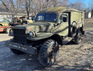 A green truck parked in the dirt near trees.